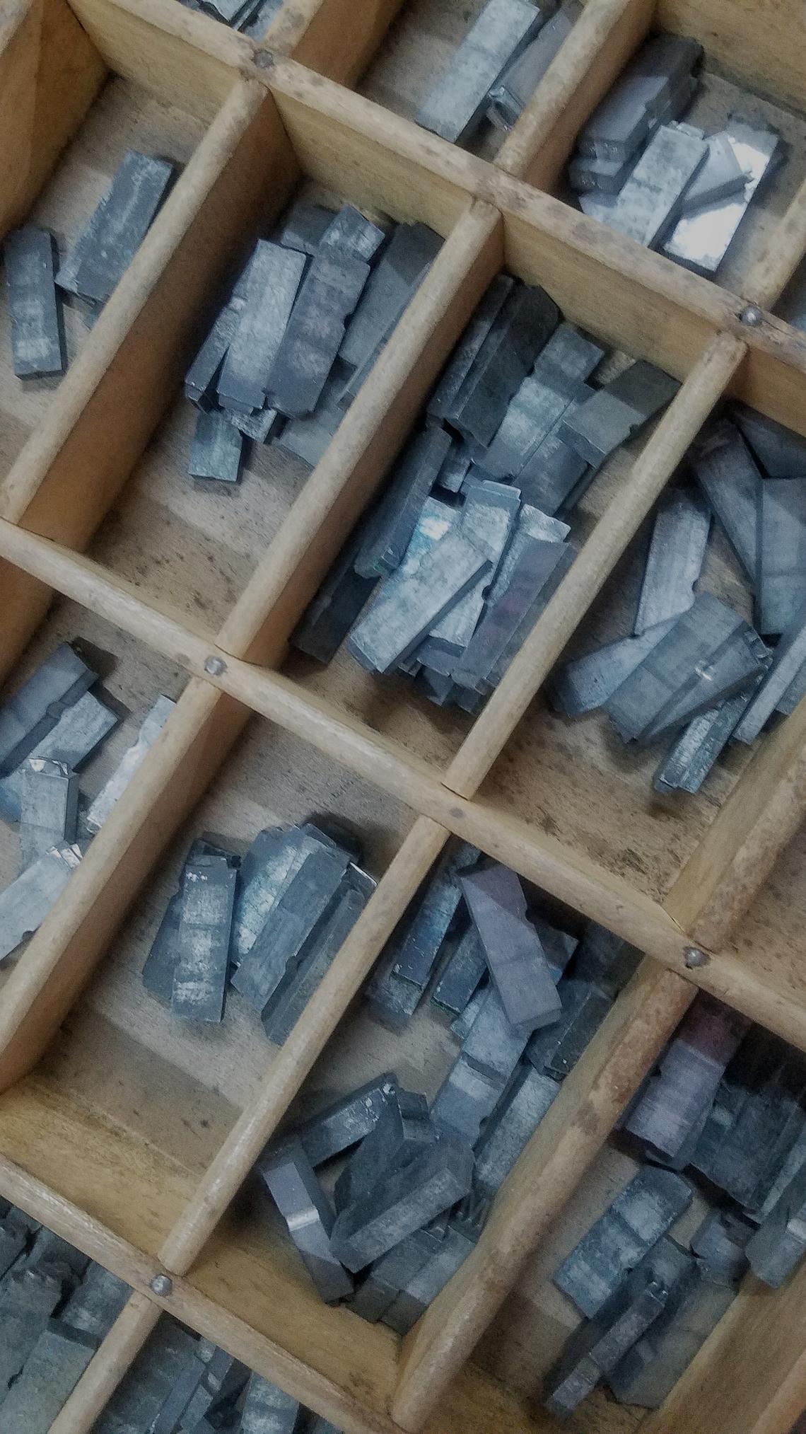 Un cajón de madera que contiene tipos móviles (esos utilizados en las imprentas tradicionales) visto de arriba en primer plano.